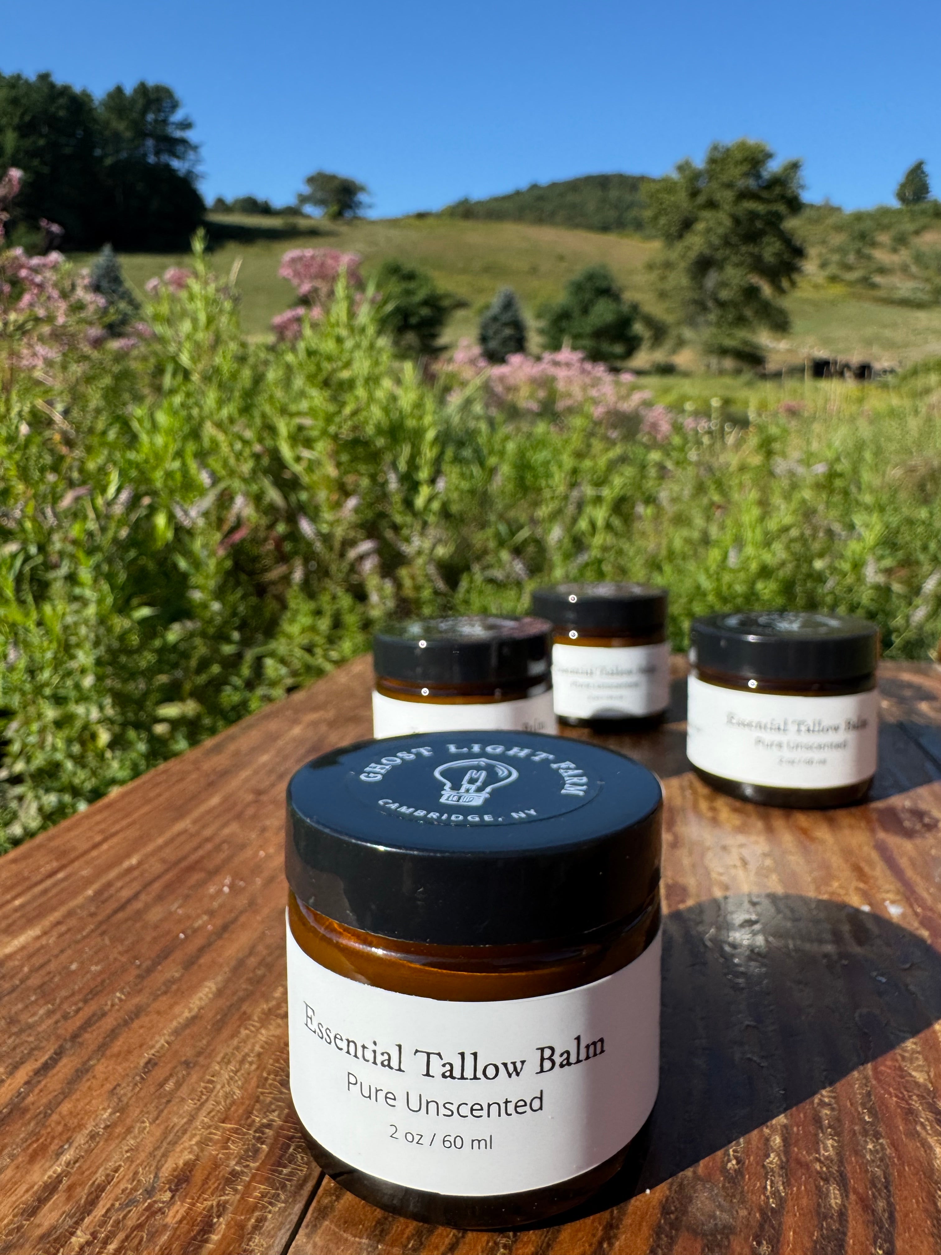Jars of tallow balm on a wooden surface with a natural landscape in the background